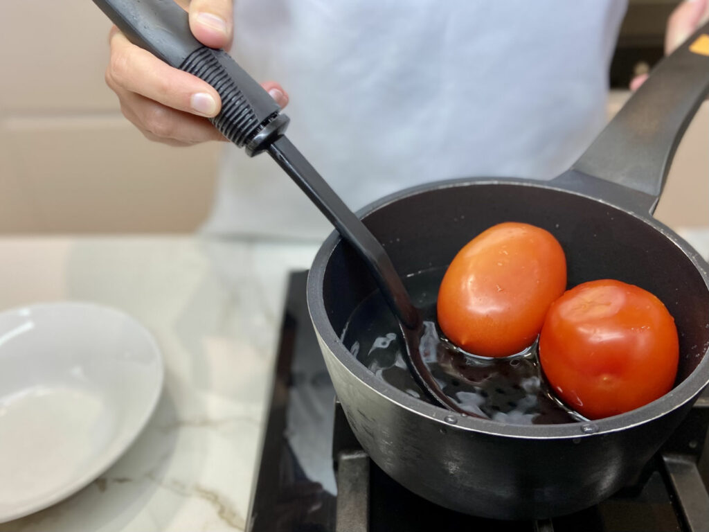olla negra con agua tomates y una cuchara