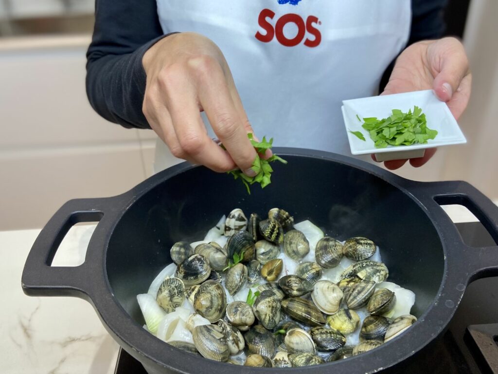 Añadimos el vino blanco y las almejas, y espolvoreamos con el perejil picado