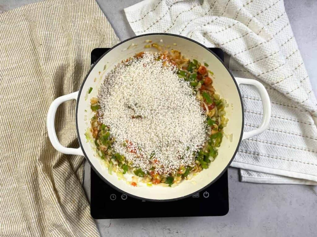 Receta de Arroz negro con calamares y gambas. Añadimos un poco de sal al sofrito y el arroz. Seguidamente, incorporamos el calamar y removemos todo muy bien.