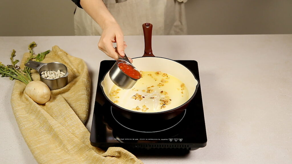 Receta tradicional valenciana de arroz en fesols y naps. Paso 3: Sofríe los dientes de ajo e incorpora el tomate triturado