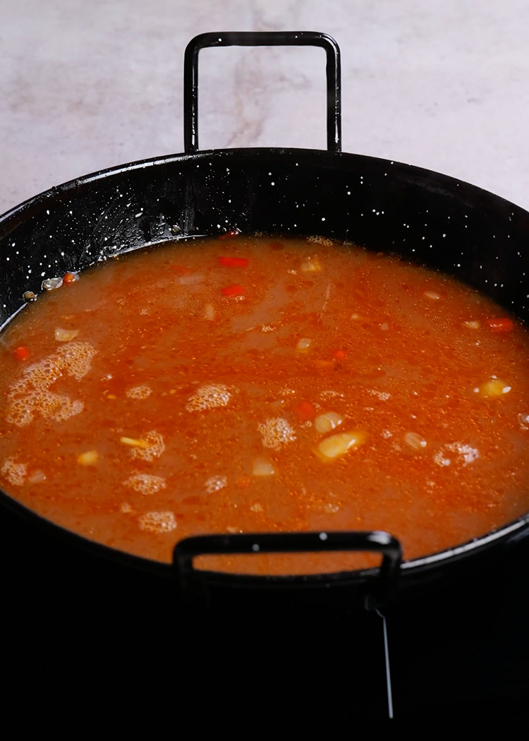Añadir caldo y especias a arroz con conejo meloso