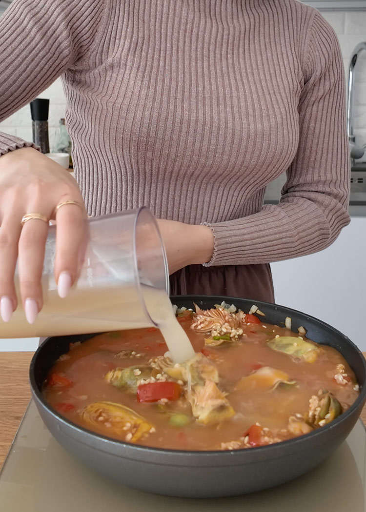 Echar caldo a arroz con alcachofas y verduras